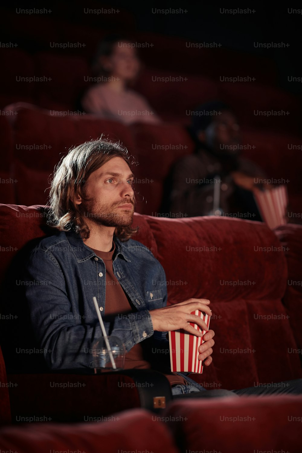 Young man concentrating on watching movie on armchair and eating popcorn in the cinema
