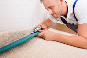 Close-up Of A Young Handyman Fitting Carpet While Installation With Cutter