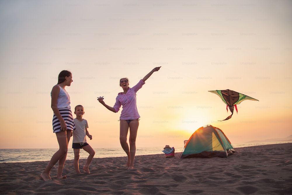 Beach Camping. Family camping and activity on the beach at sunset. Mother and child flying kite at beach