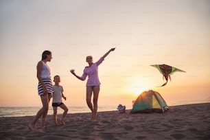 Campeggio sulla spiaggia. Campeggio per famiglie e attività sulla spiaggia al tramonto. Aquilone volante della madre e del bambino alla spiaggia