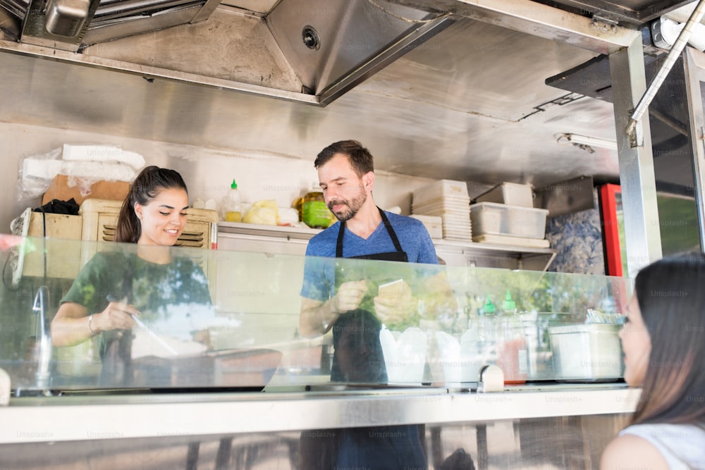 Man and woman cooking and serving some food to a female diner in a food stand