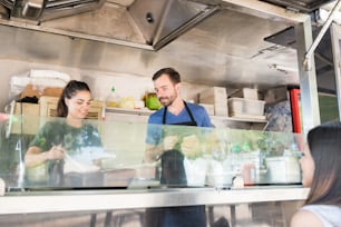 Man and woman cooking and serving some food to a female diner in a food stand