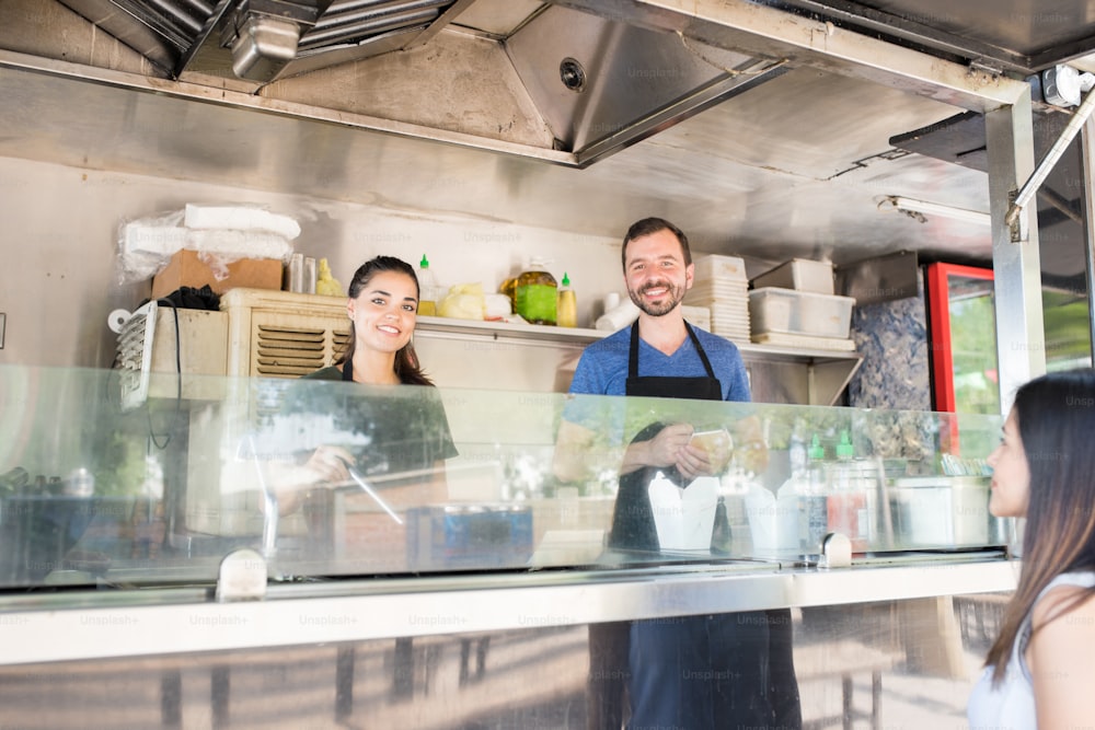 Portrait of a couple of food truck owners working and cooking some food for a customer