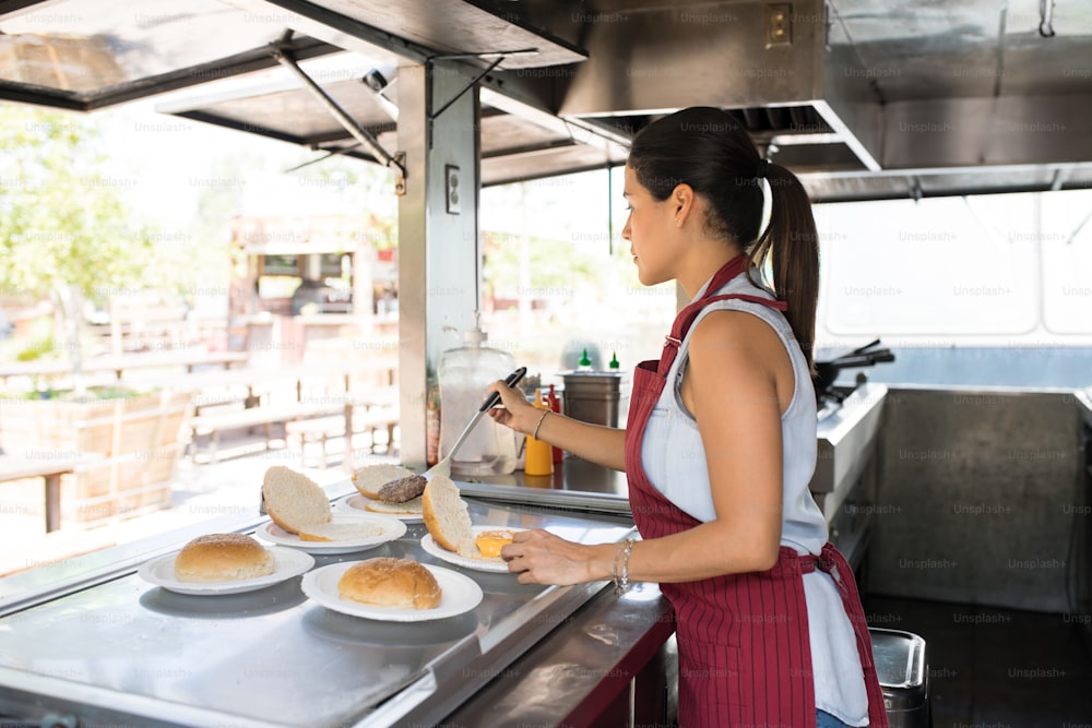 Vista del profilo di una cuoca latina che lavora in un camion di cibo e prepara alcuni hamburger