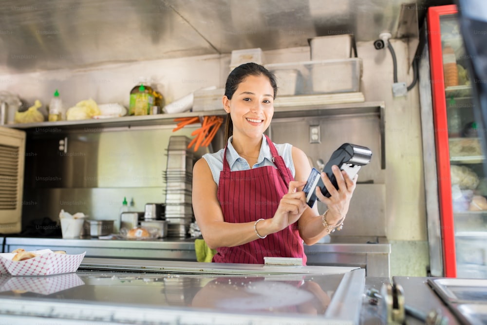 Schöne hispanische Food-Truck-Arbeiterin, die mit einer Kreditkarte bezahlt wird und lächelt