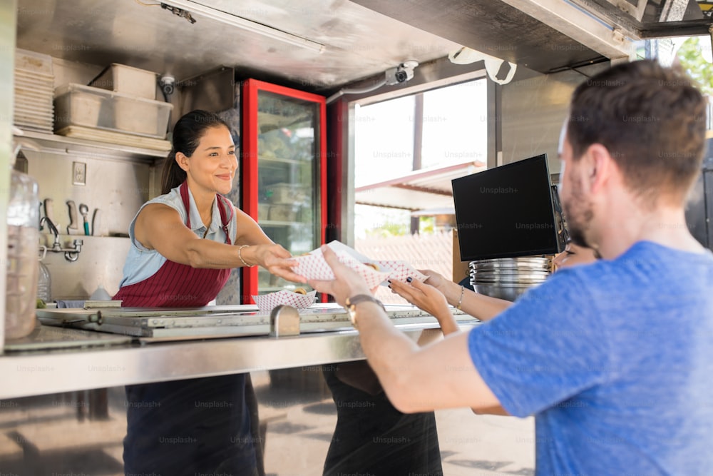 Cute young female cook selling hot dogs to a couple of customers in a food stand