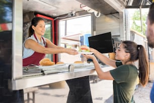 Vista de perfil de un trabajador de un camión de comida entregando una hamburguesa a un cliente y sonriendo
