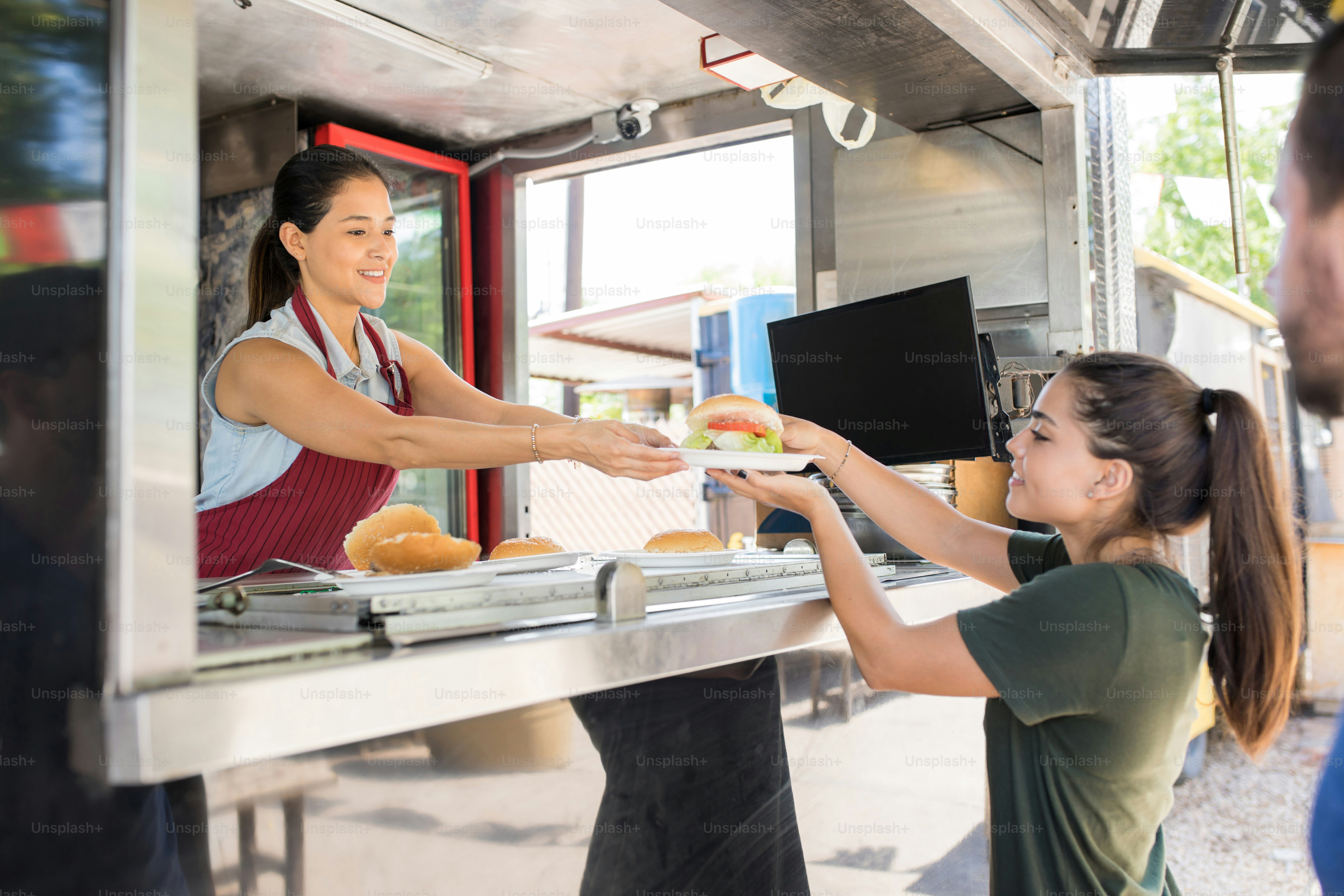 Profile view of a food truck worker handing over a hamburger to a customer and smiling