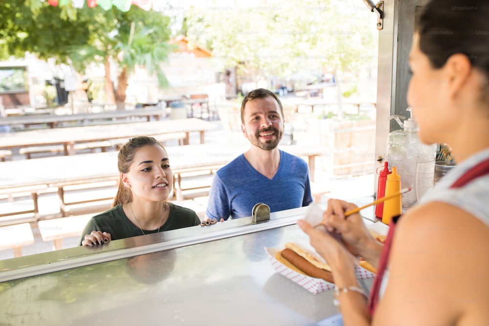 Point of view of a female worker in a food truck writing down orders from her customers