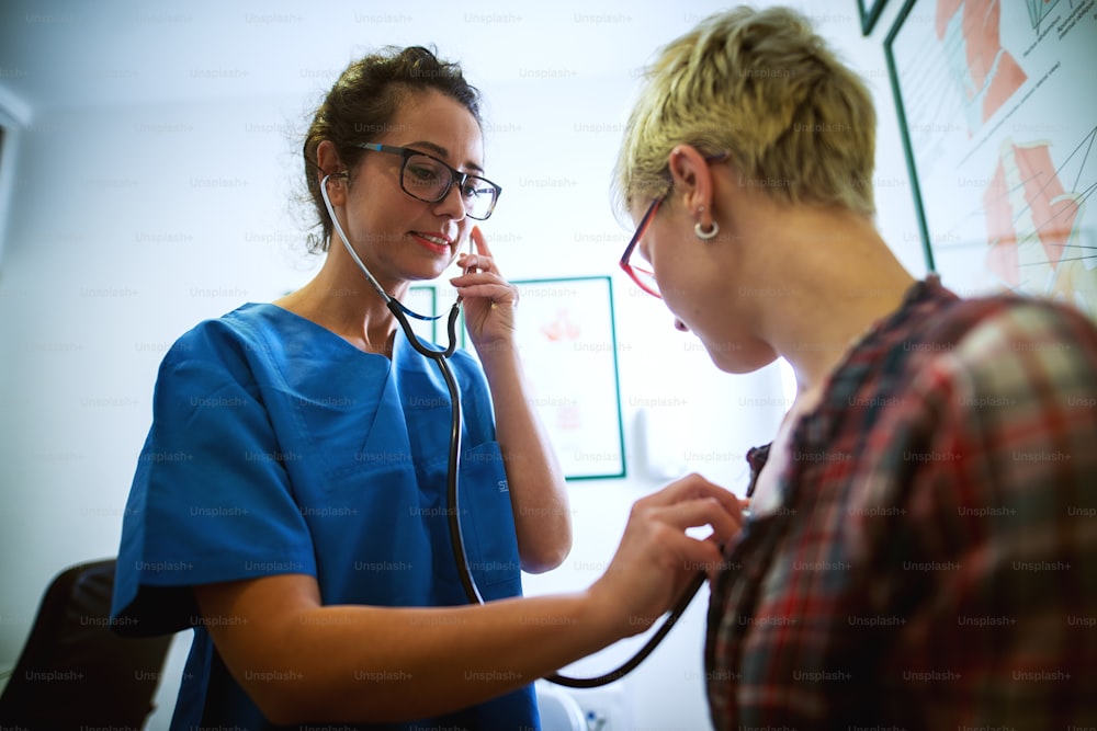 Portrait d’une infirmière professionnelle d’âge moyen vérifiant l’état de santé d’une patiente avec un stéthoscope au bureau.