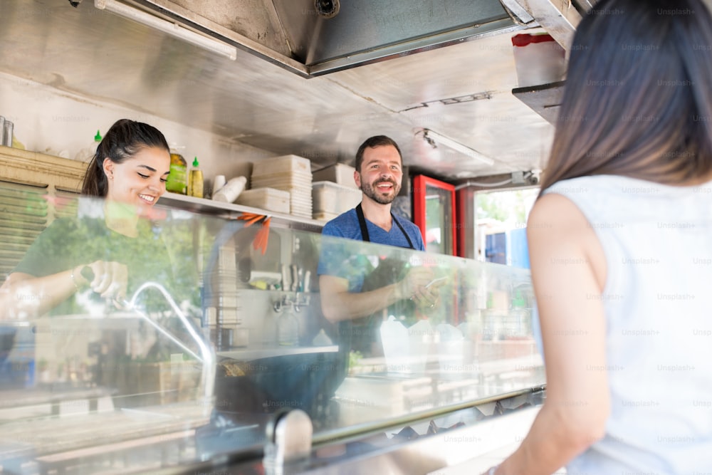 Good looking man taking the order of a woman while cooking some food in a food truck