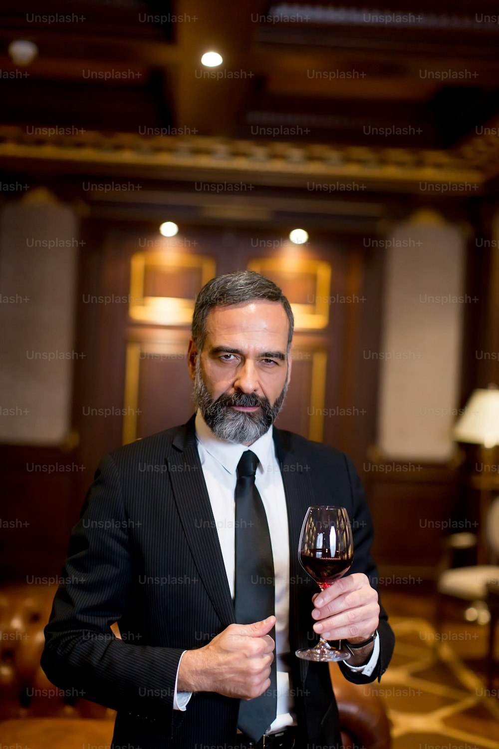 Bello uomo d'affari elegante che beve vino rosso nel bar