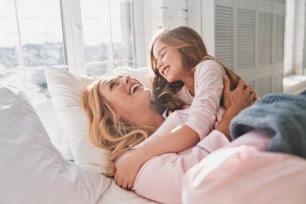 Giovane bella madre con la sua piccola figlia carina sorridente mentre si trova sul letto a casa