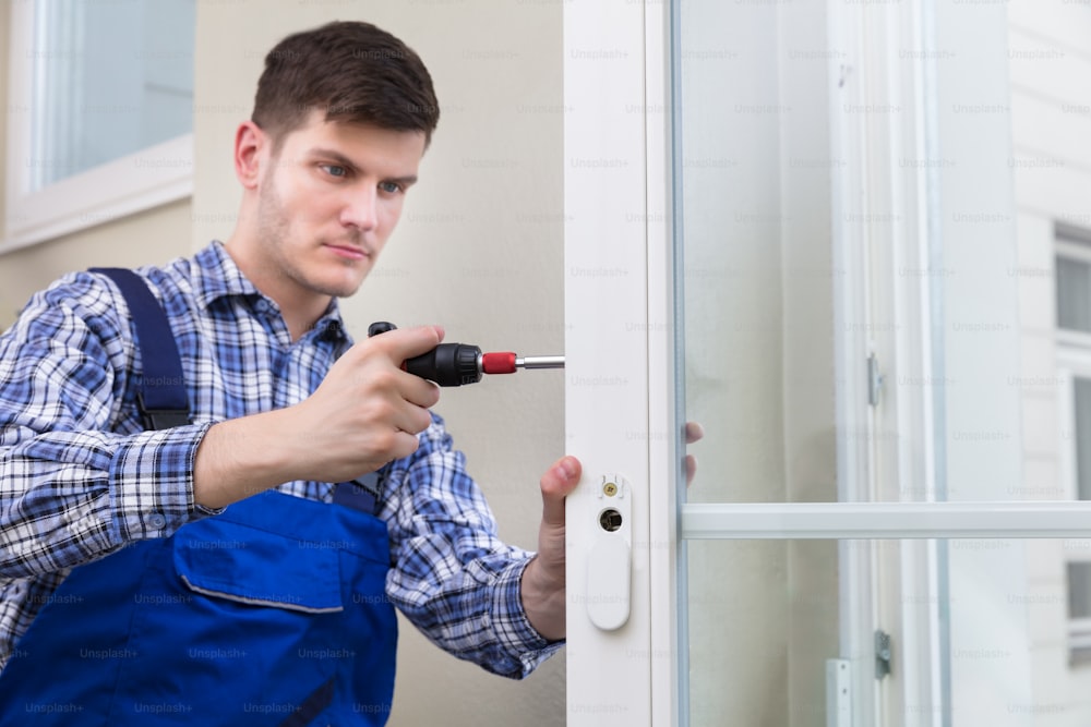 Male Handyman In Uniform Fixing Glass Window With Screwdriver