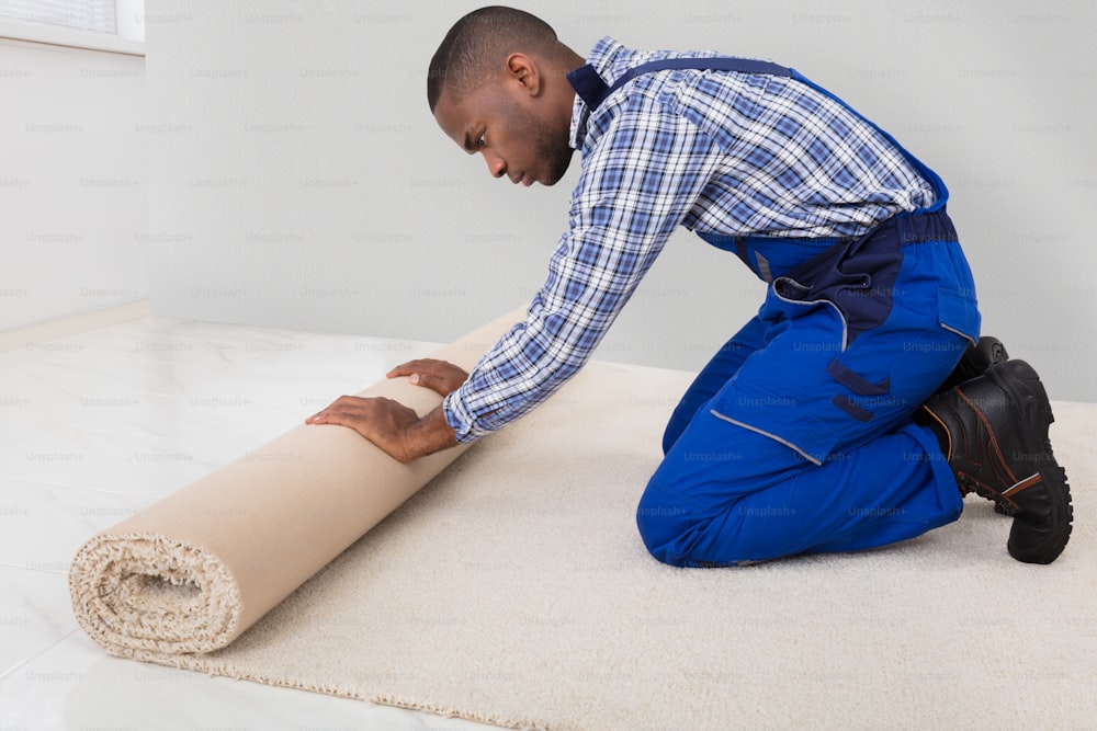 Young Male Handyman Rolling Carpet On Floor At Home