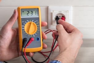 Nahaufnahme der Hände des Elektrikers, die die Spannung der Steckdose mit einem Multimeter im Haus überprüfen