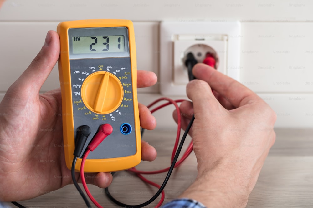 Close-up Of Electrician's Hands Checking Voltage Of Socket With Multimeter In House