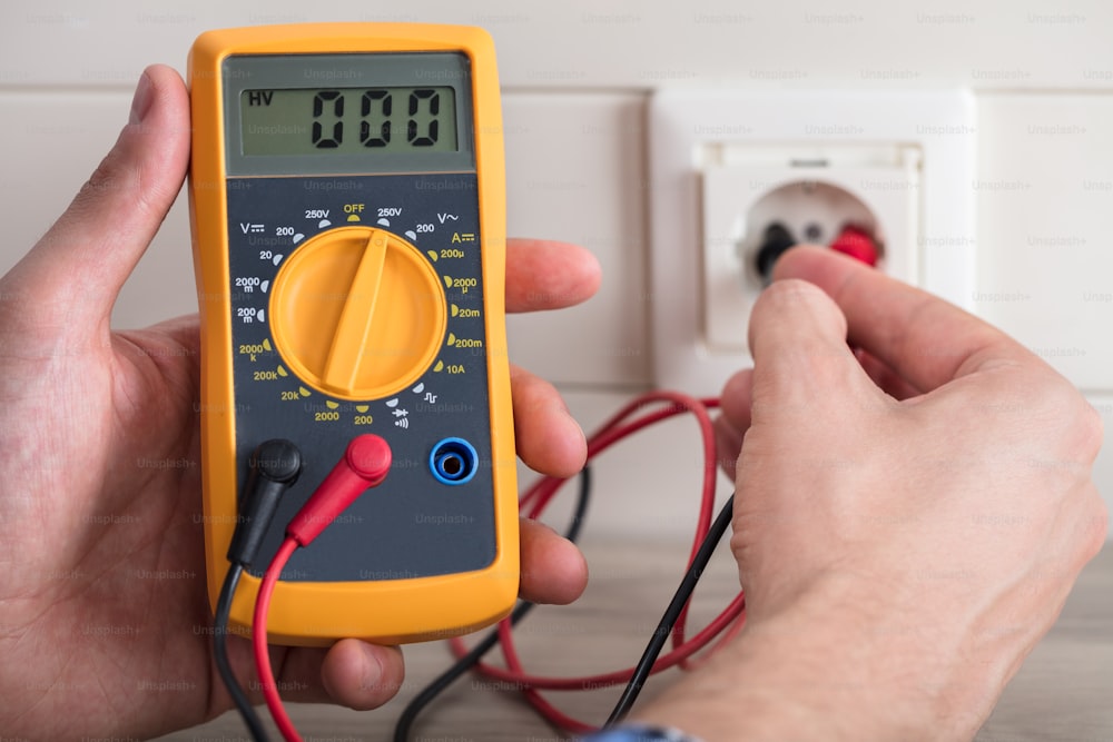 Close-up Of Human Hand And Metering Socket Voltage With Digital Multimeter