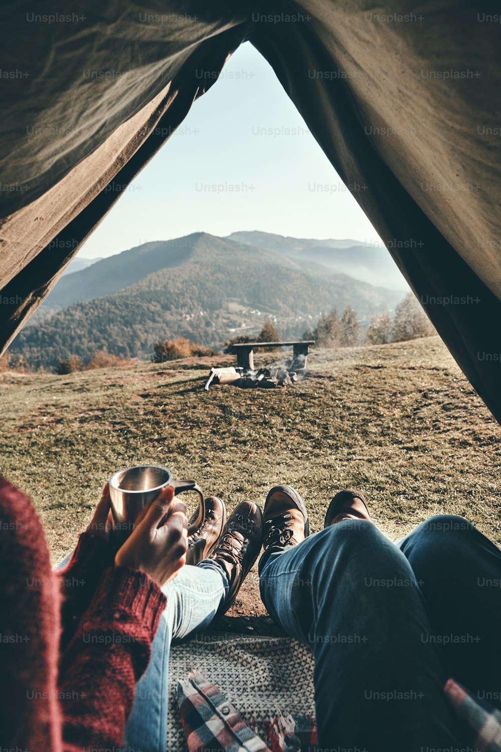 Nahaufnahme eines jungen Paares, das morgens Kaffee trinkt, während es von seinem Zelt aus den Blick auf die Bergkette genießt