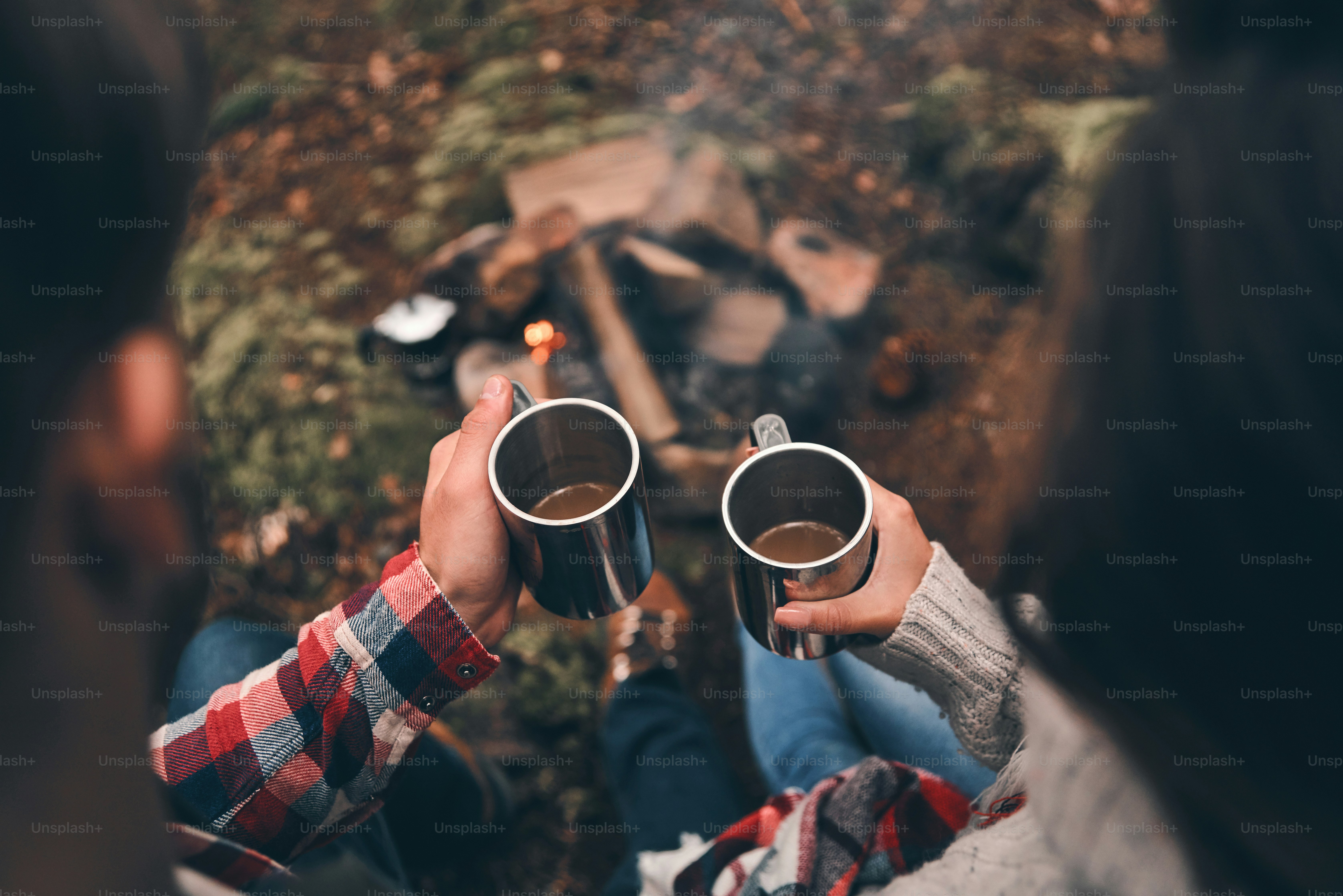 Close up top view of young couple holding cups while warming up near the campfire