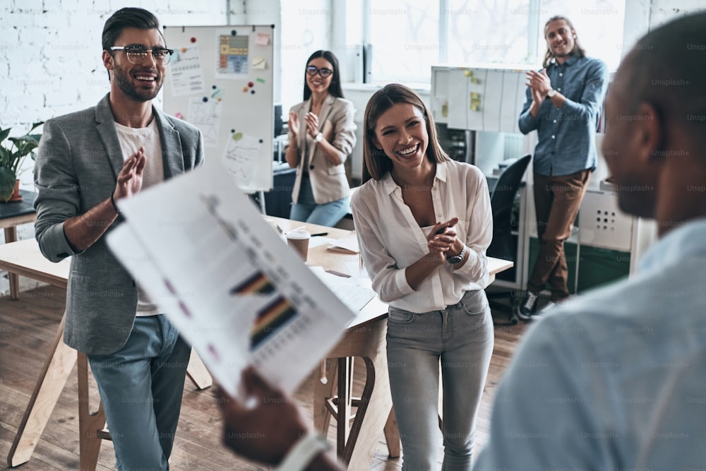 Gruppo di uomini d'affari che applaudono e sorridono mentre lavorano nella sala del consiglio di amministrazione