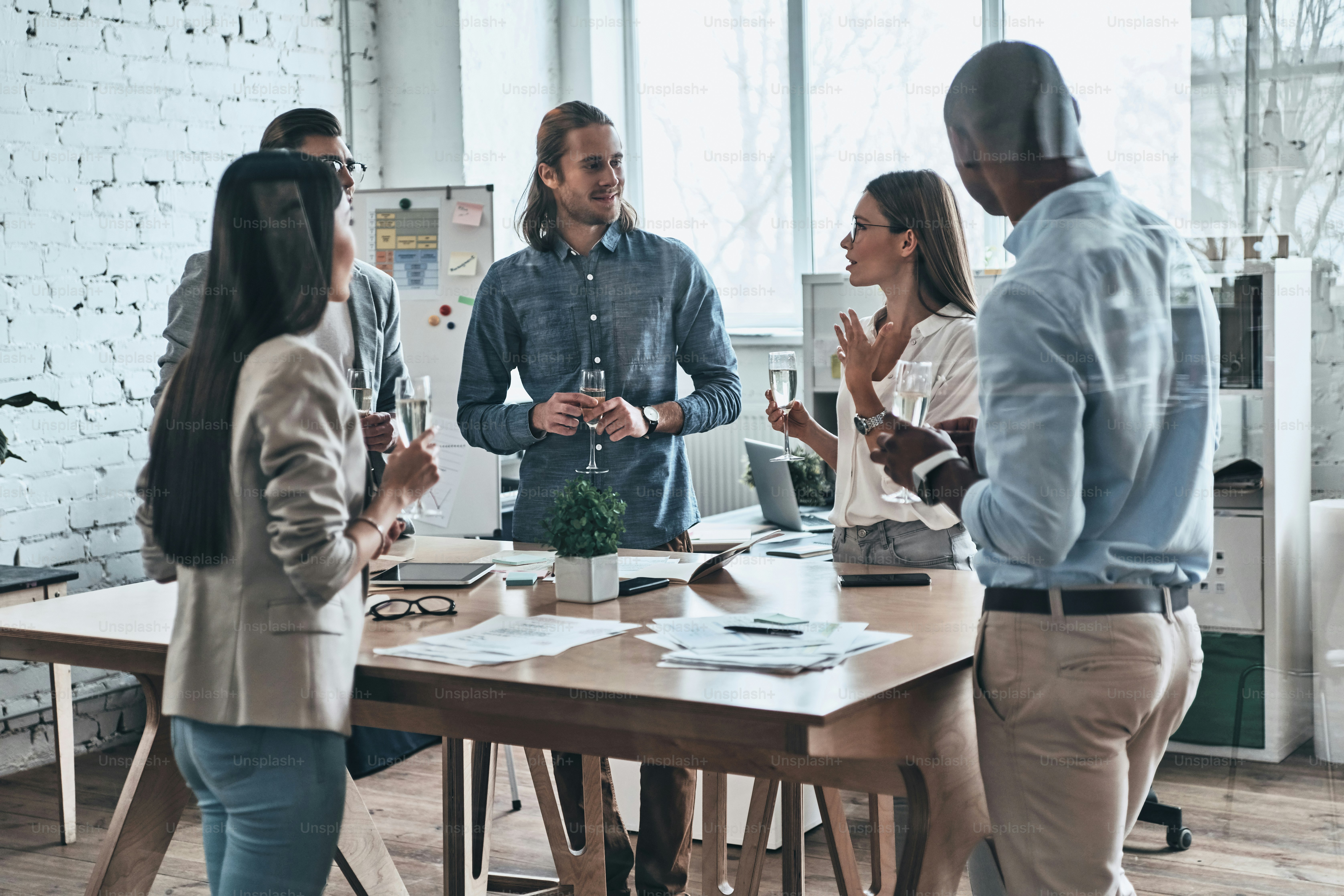 Diverse group of young business people drinking champagne and smiling while standing in the board room