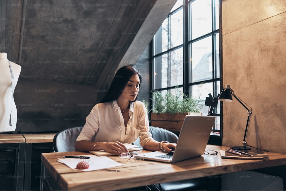 Concentrated young woman using laptop while sitting in her workshop