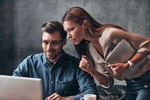 Two young colleagues in smart casual wear discussing something while spending time in the office