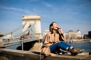 Mujer joven usando un teléfono móvil con el puente de las Cadenas al fondo en Budapest, Hungría