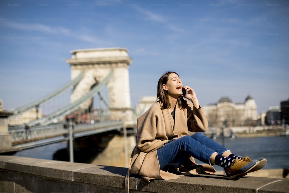 Mujer joven usando un teléfono móvil con el puente de las Cadenas al fondo en Budapest, Hungría