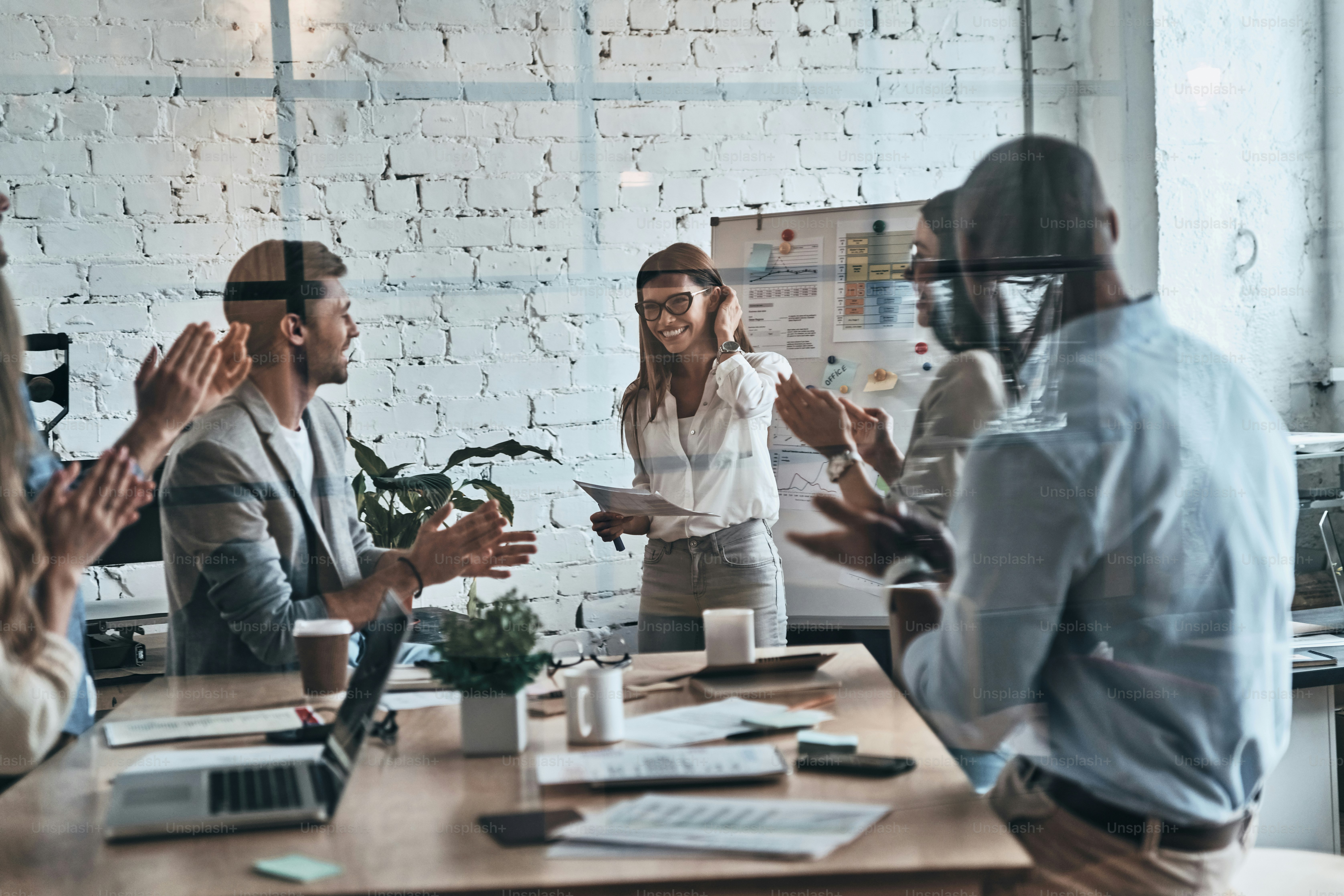Modern young business people clapping and smiling while working behind the glass wall in the board room