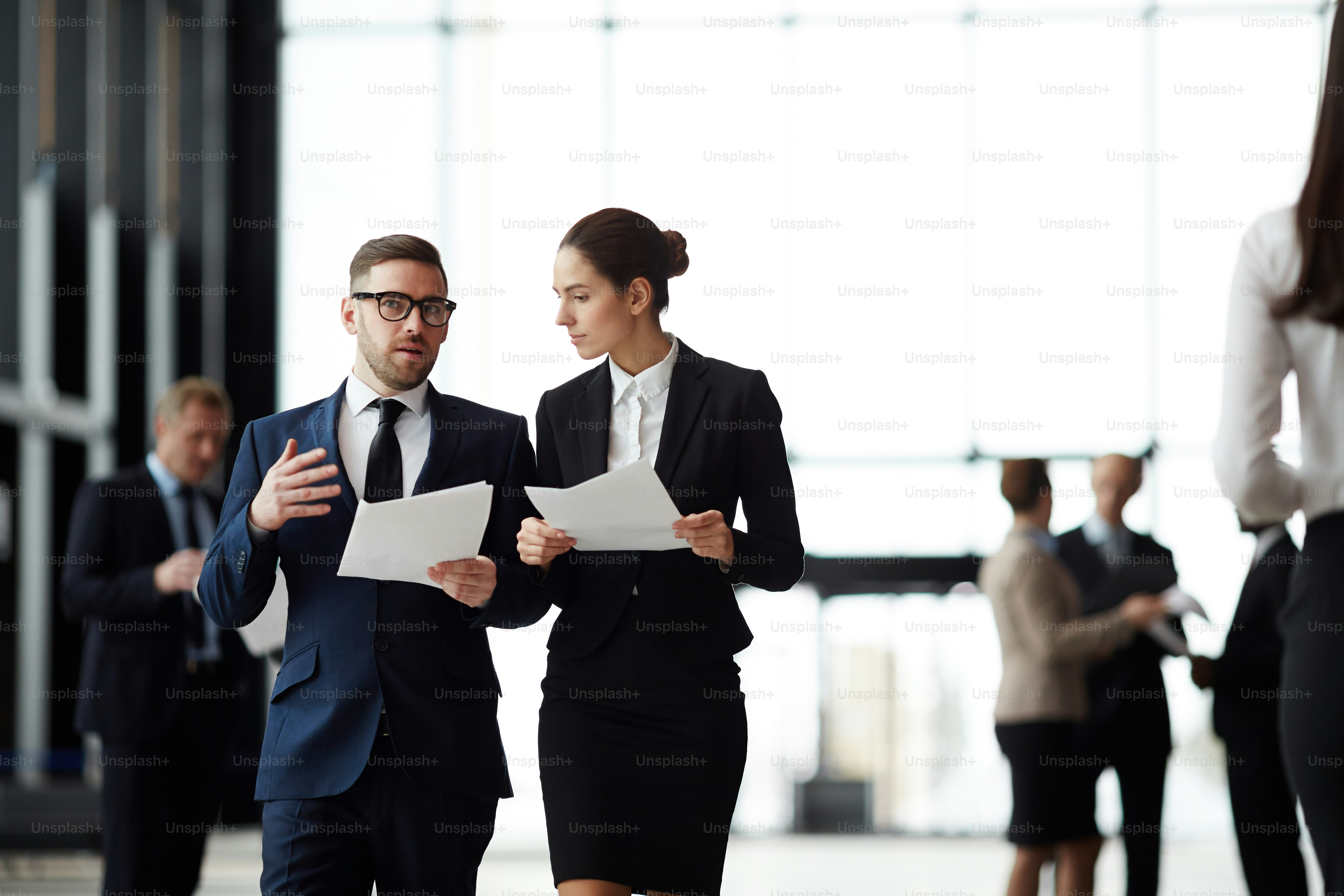 Businessman with papers consulting with young female colleague while walking to conference