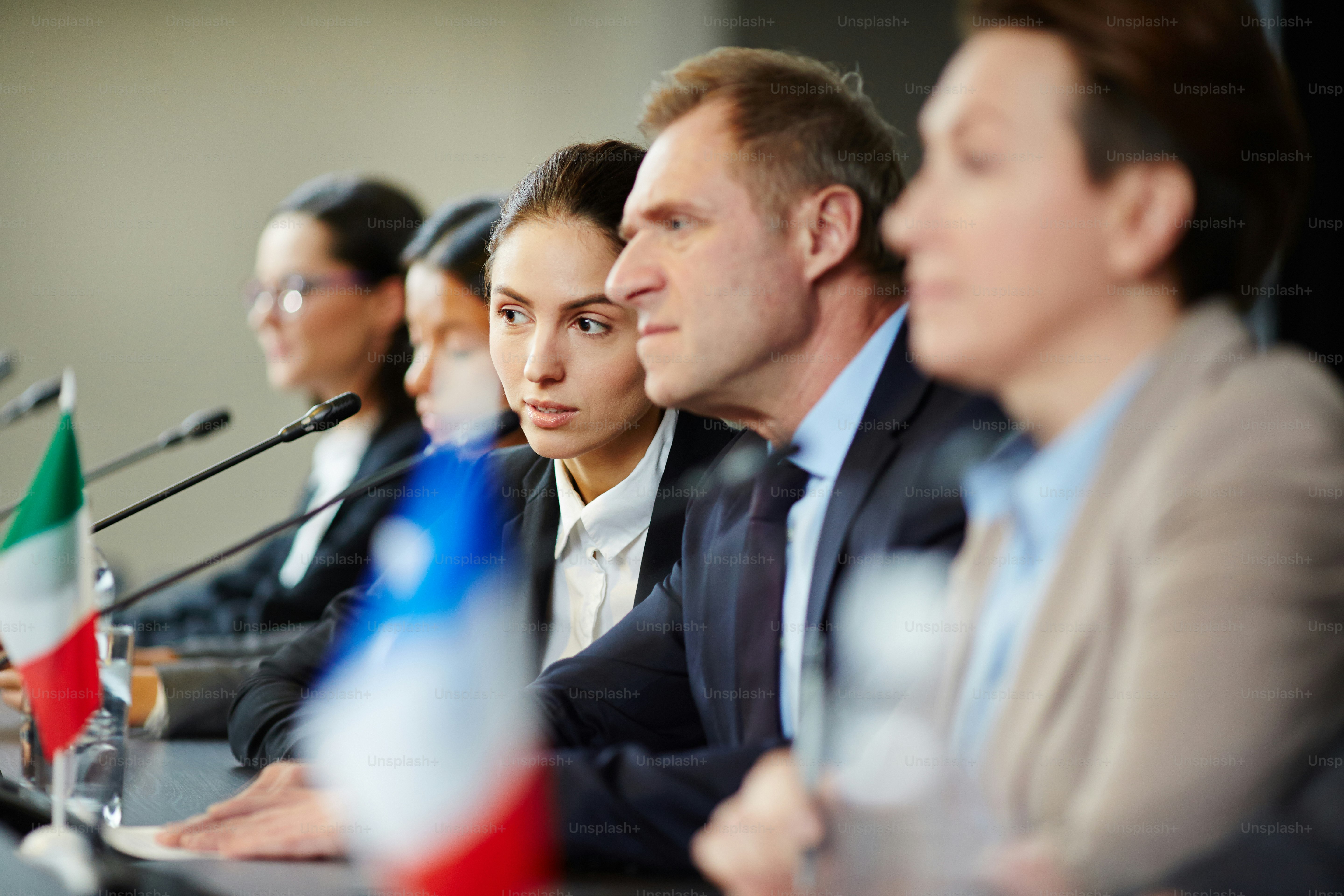 One of young speakers consulting with mature delegate while listening to other participants of conference