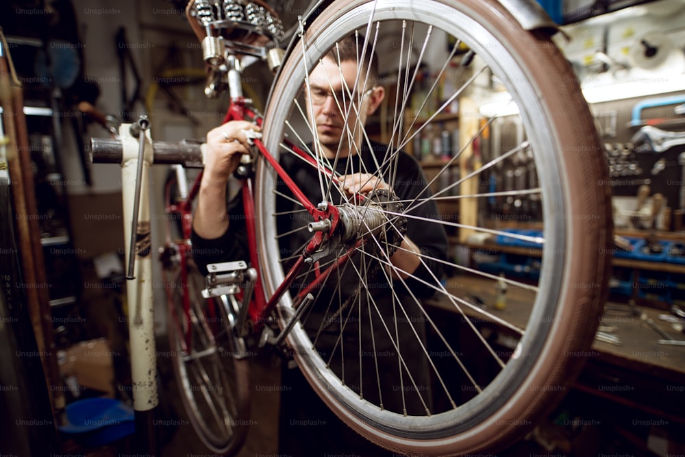 Professional young man cleaning bicycle rear bar in the workshop.