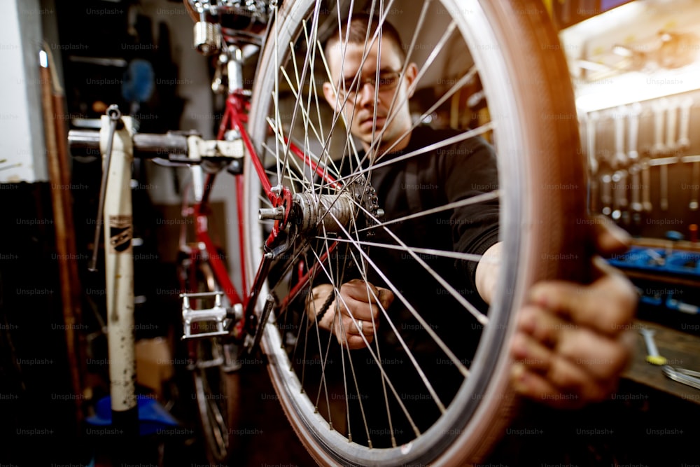 Jovem profissional ajustando firmemente os fios das rodas da bicicleta.