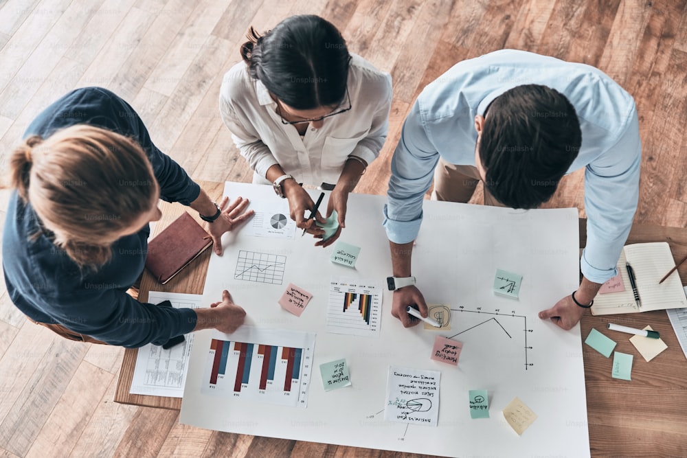 Close up top view of young confident business people working together while man writing on blueprint in the office