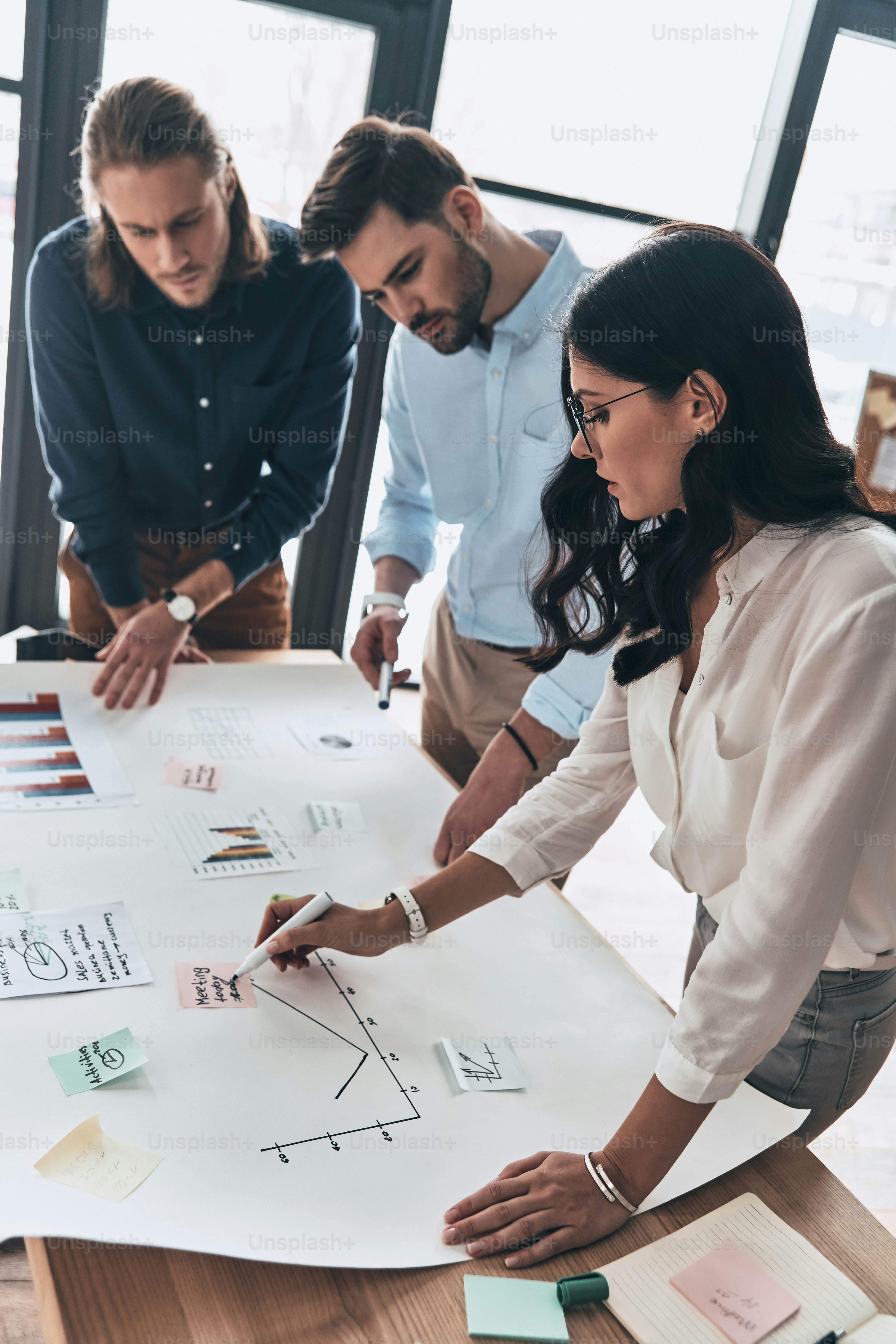 Top view of young confident business people discussing something while working with blueprint in the office