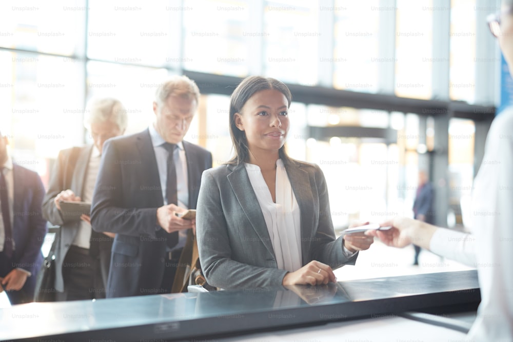 Happy mixed-race businesswoman giving her documents to check-in manager by counter in airport