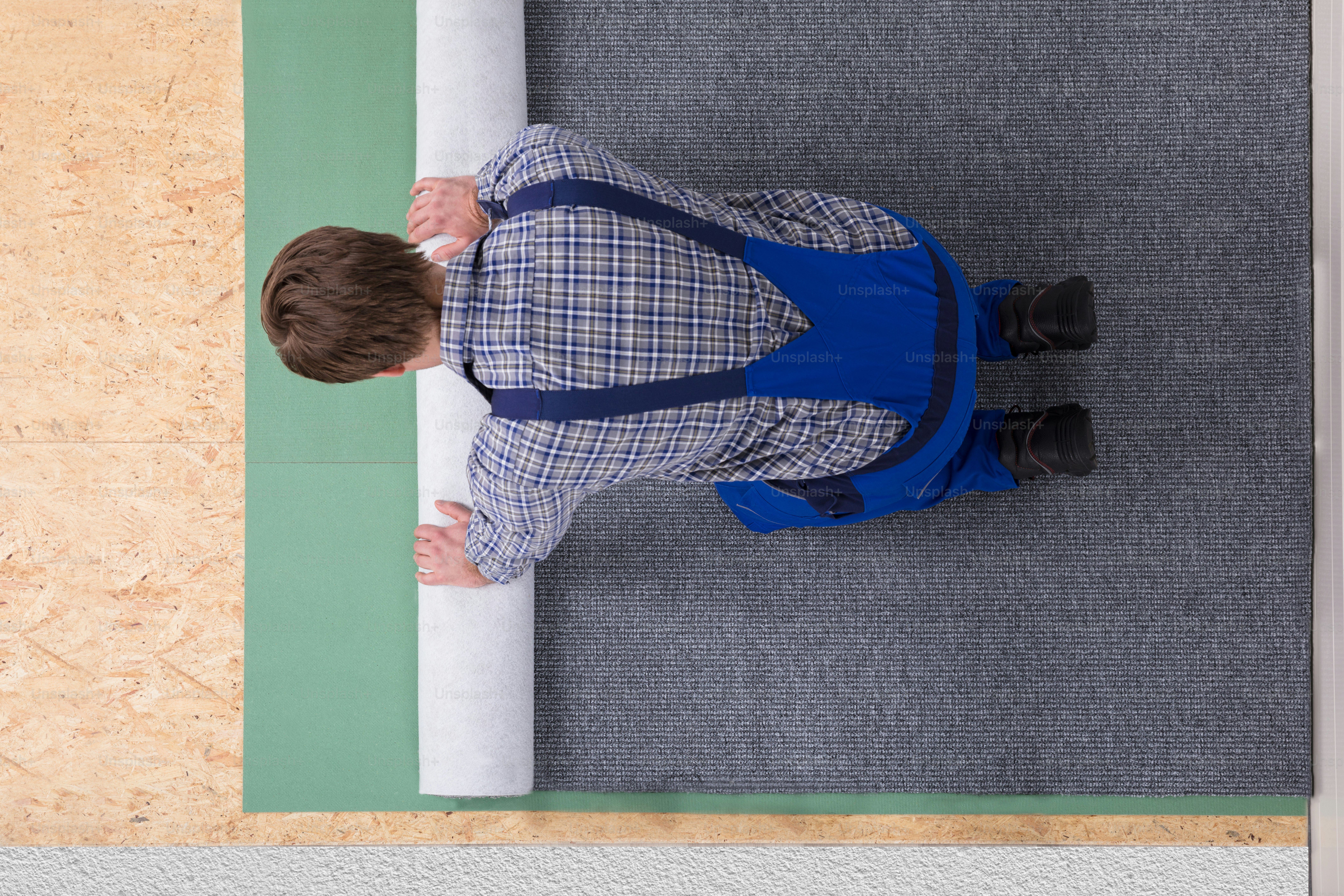 Side View Of A Young Male Worker In Overalls Installing Carpet
