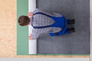 Side View Of A Young Male Worker In Overalls Installing Carpet