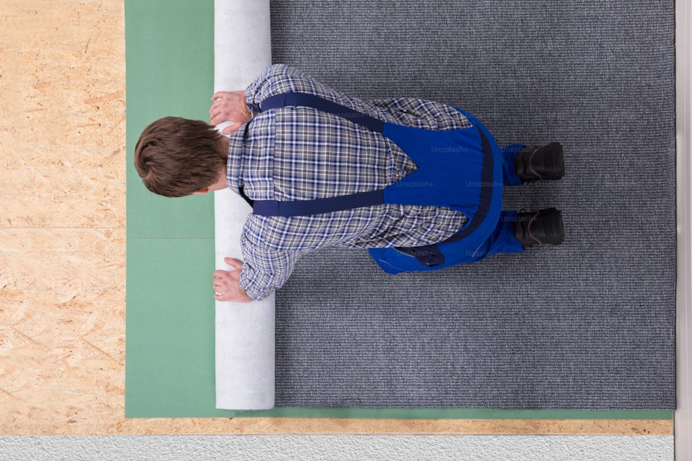 Seitenansicht eines jungen männlichen Arbeiters in Overalls, der Teppich installiert