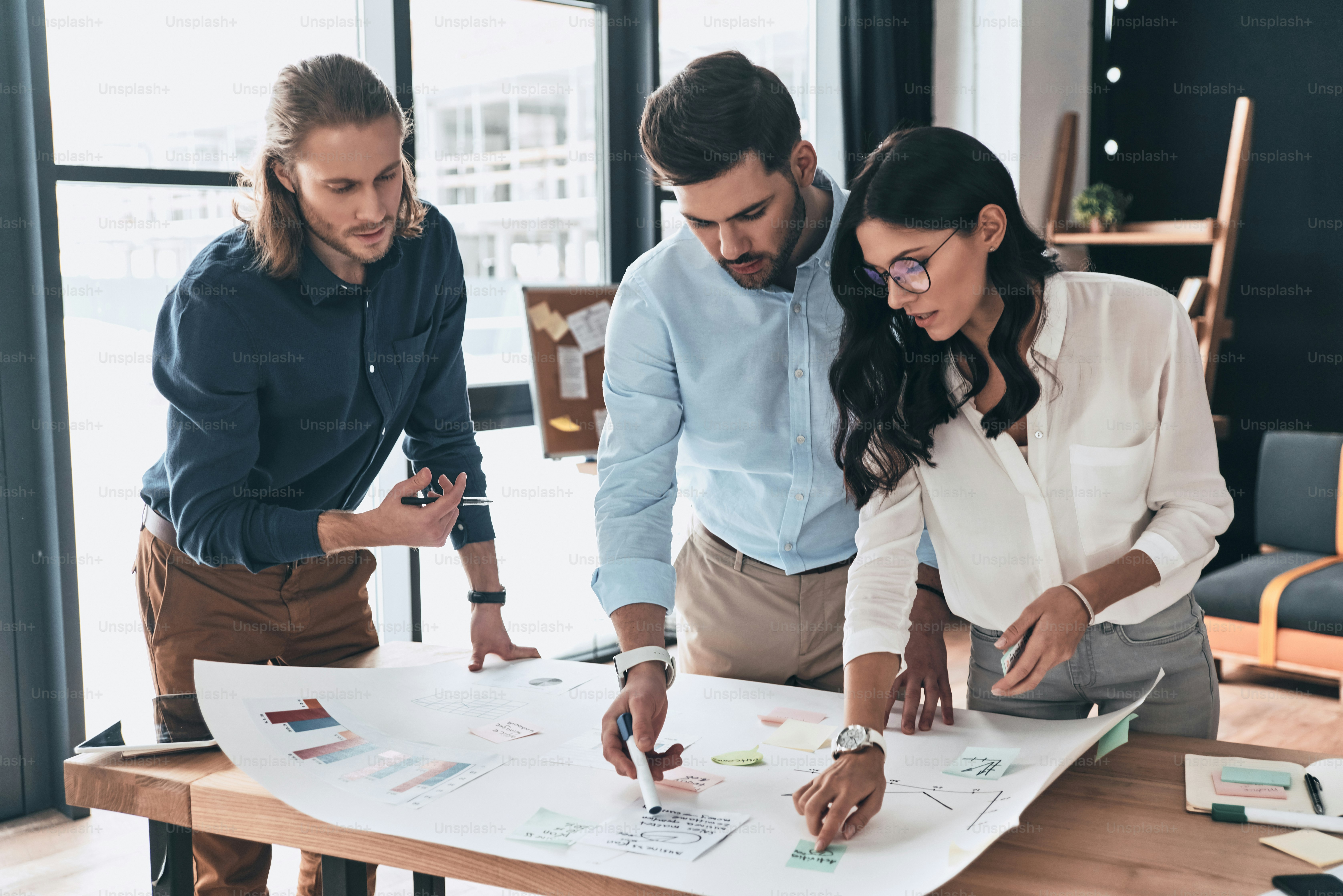 Group of young confident business people discussing something while looking at blueprint in the office