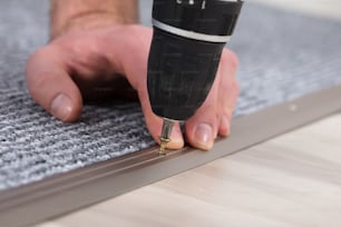 Primer plano de la mano de un instalador de alfombras instalando alfombra gris con destornillador inalámbrico