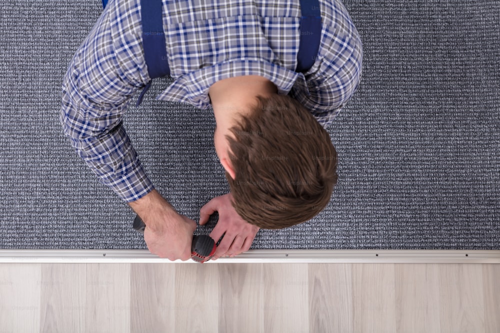 Close-up Of A Carpet Fitter's Hand Installing Grey Carpet With Wireless Screwdriver