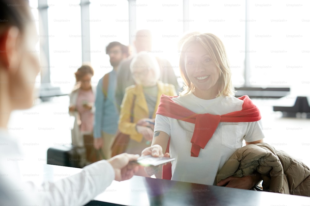 Happy traveler taking back her documents after check-in at registration counter in airport before departure