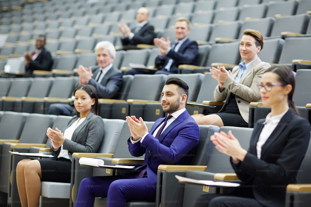 Happy audience clapping hands after speech or presentation of colleague at business conference
