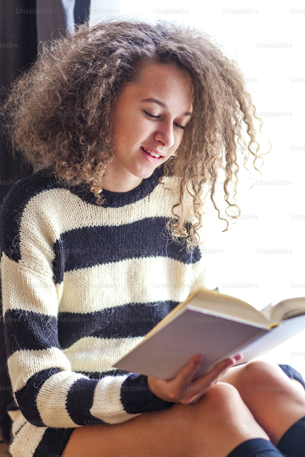 Curly hair teen girl reading book by window