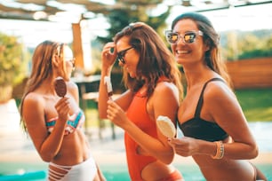 Portrait of three female friends eating icecream by pool in summer