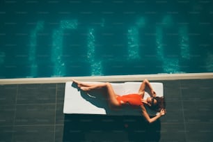 Mulher nova deitada na piscina no dia quente de verão