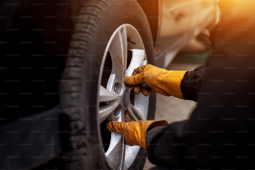 Homem mecânico de automóveis com chave de fenda elétrica trocando pneu do lado de fora. Serviço de carro. As mãos substituem os pneus nas rodas. Conceito de instalação de pneus.